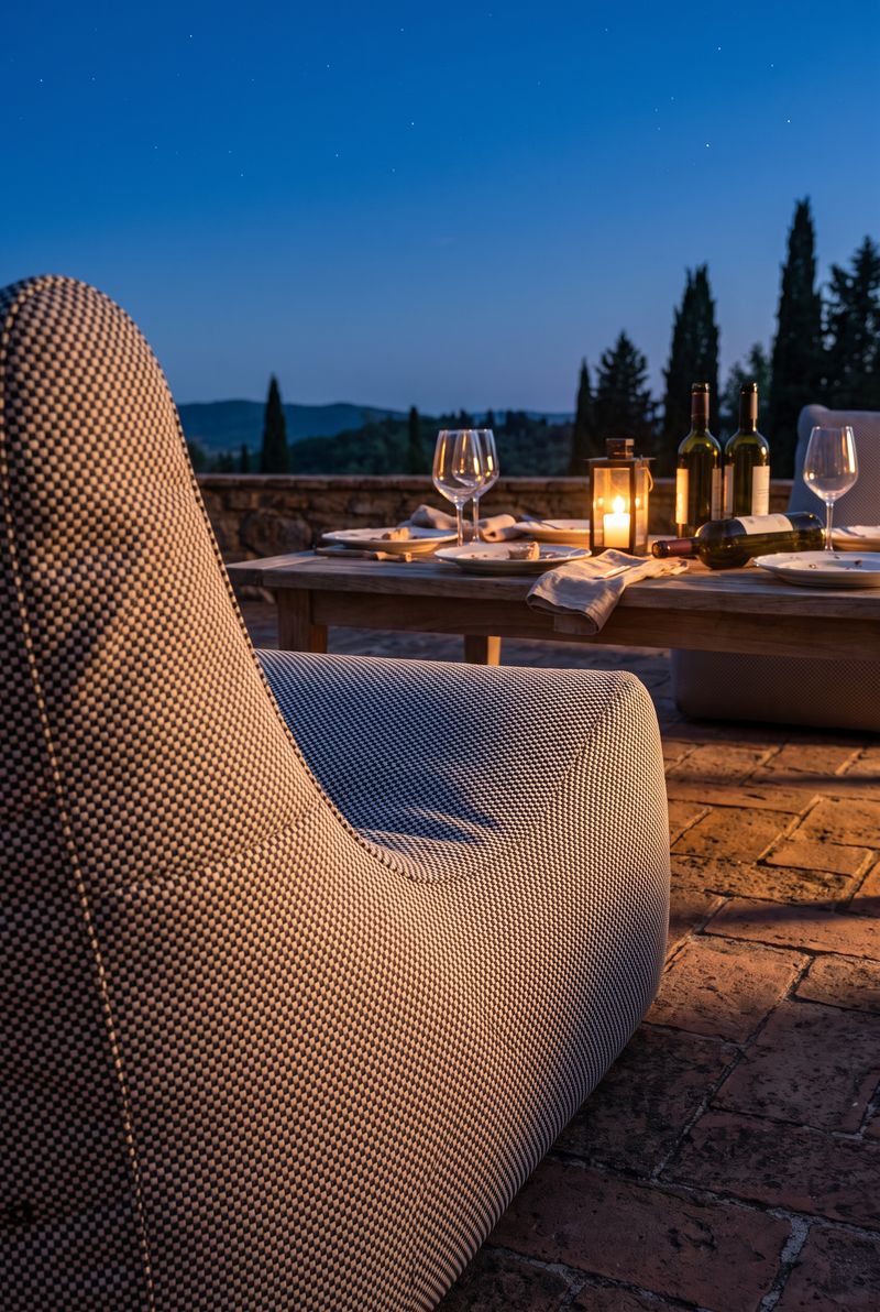 Outdoor-Loungesessel auf einer Terrasse in der Daemmerung, gedeckter Tisch mit Laterne, Huegellandschaft im Hintergrund