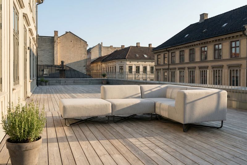 Beiges Outdoor-Ecksofa auf einer Holzterrasse ueber den Daechern einer Altbaustrasse