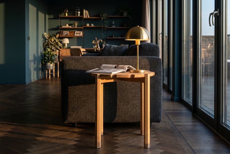 Beistelltisch aus Holz neben einem dunklen Polstersessel, Messinglampe und aufgeschlagenes Buch im Abendlicht