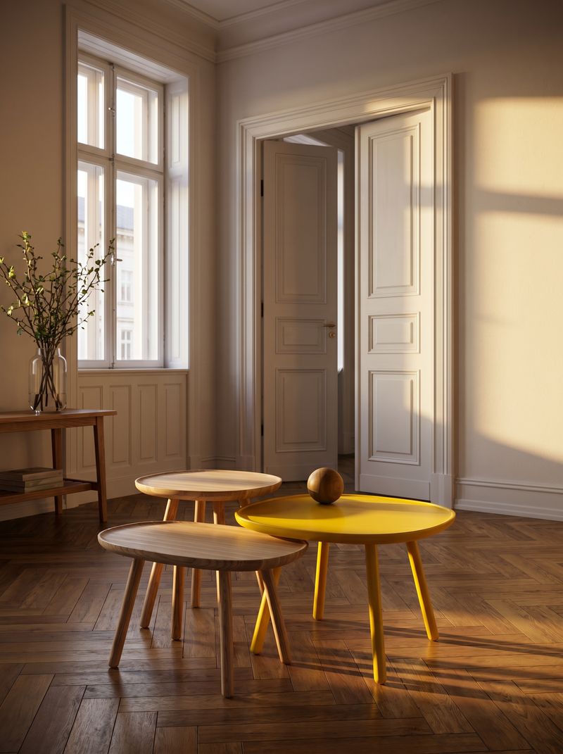 Draufsicht auf drei verschachtelte runde Beistelltische in Holz, Weiß und Gelb auf Fischgrätparkett, mit Kaffeetasse und Designmagazin